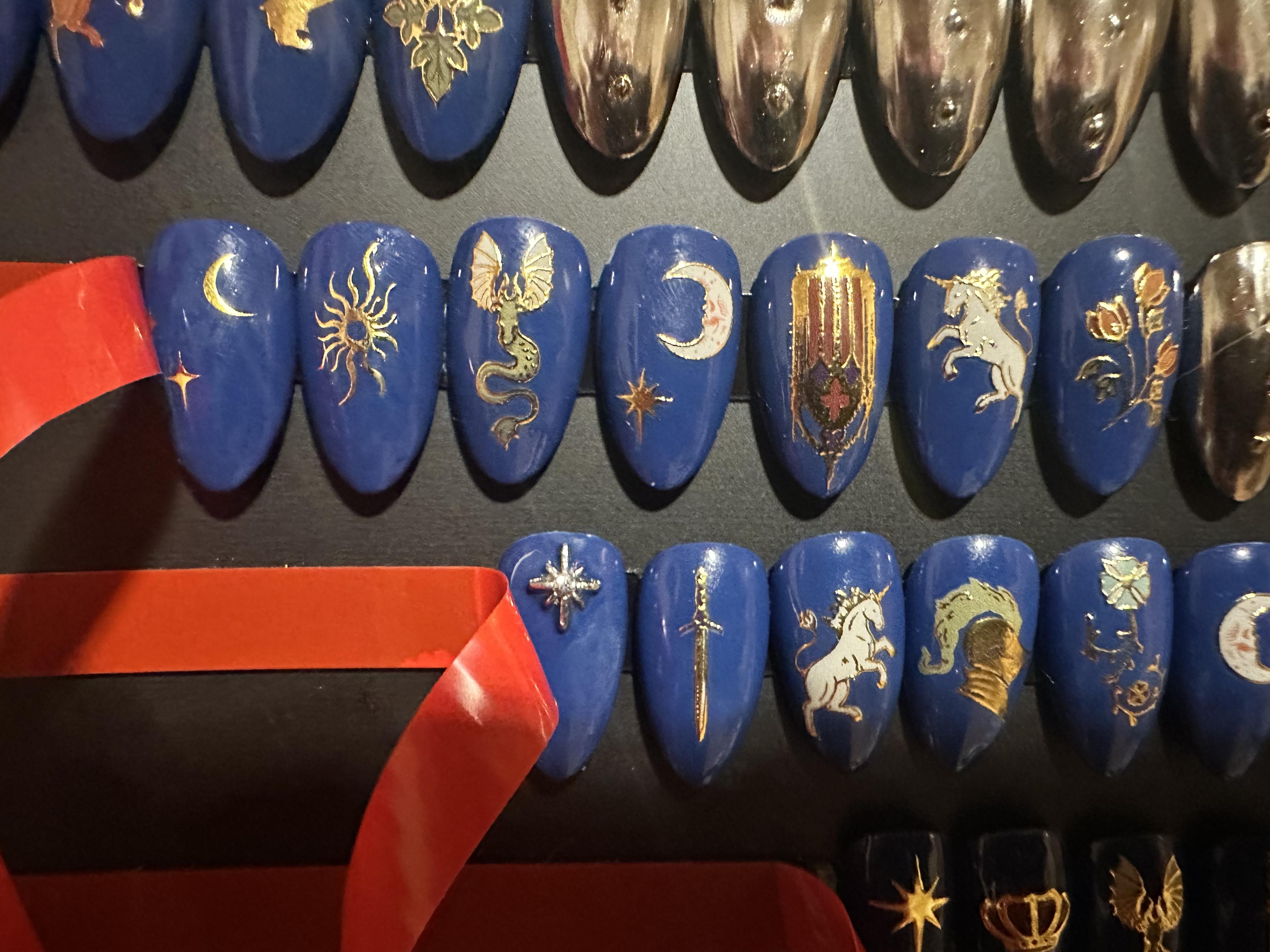 Blue medieval nails with gold dragons, suns, and unicorns